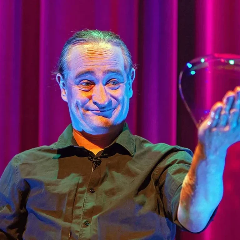 Een man houdt een zeepbel in zijn hand en lacht tegen een kleurrijke achtergrond.
