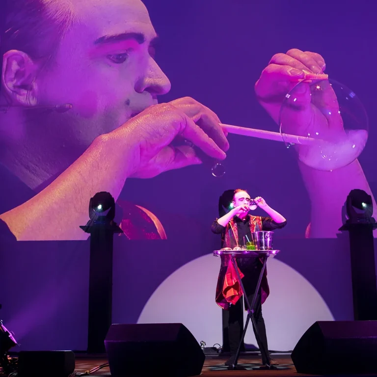 Een artiest blaast zeepbellen op een podium met paarse verlichting.