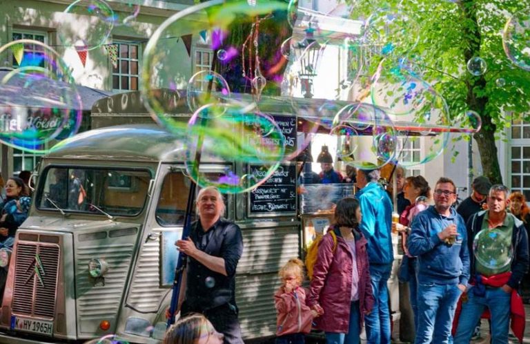 Reuzenzeepbellen rond een menigte en een oude foodtruck op een feestje.