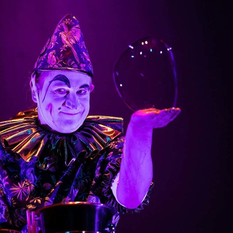 Clown in feestelijk tenue houdt een glinsterende zeepbel in zijn hand.