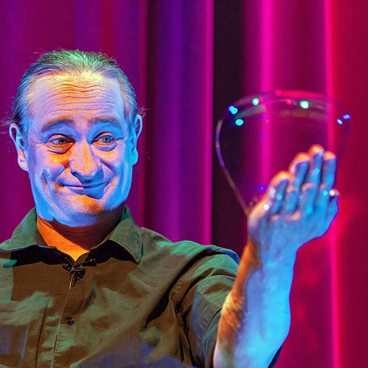 Een man houdt een grote zeepbel in zijn hand tegen een kleurrijke achtergrond.