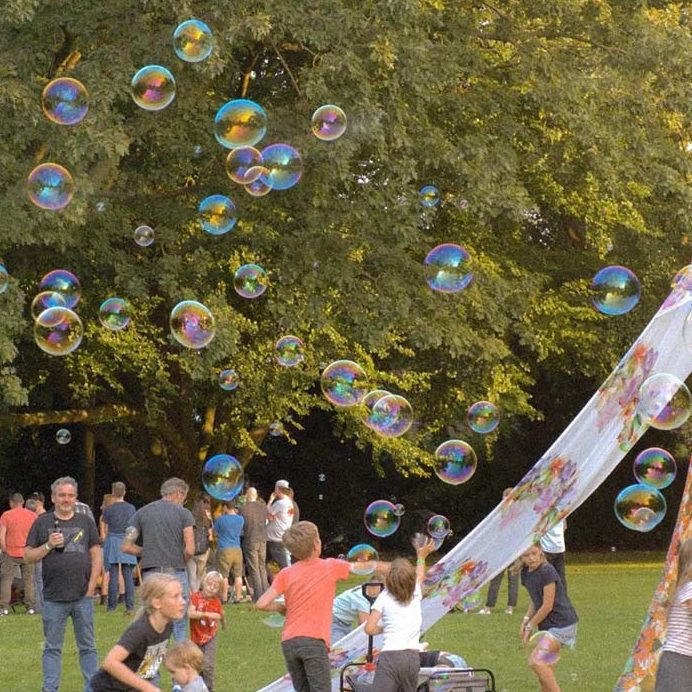 Kinderen spelen met zeepbellen in een park vol mensen en bomen.