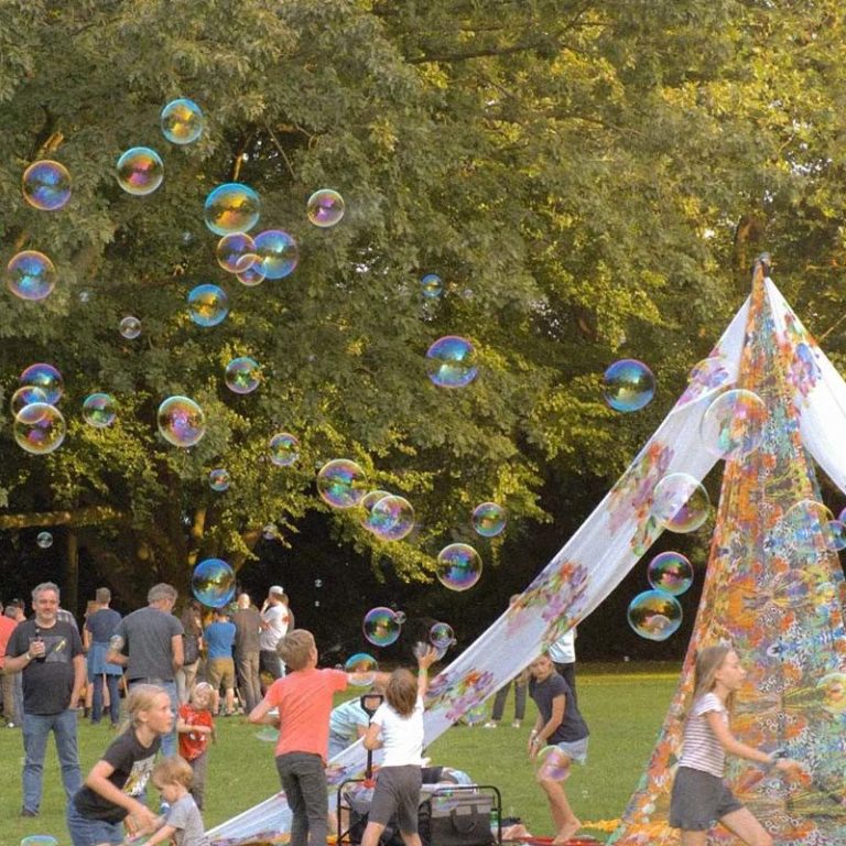 Kinderen spelen met zeepbellen naast een kleurrijke tent in het park.