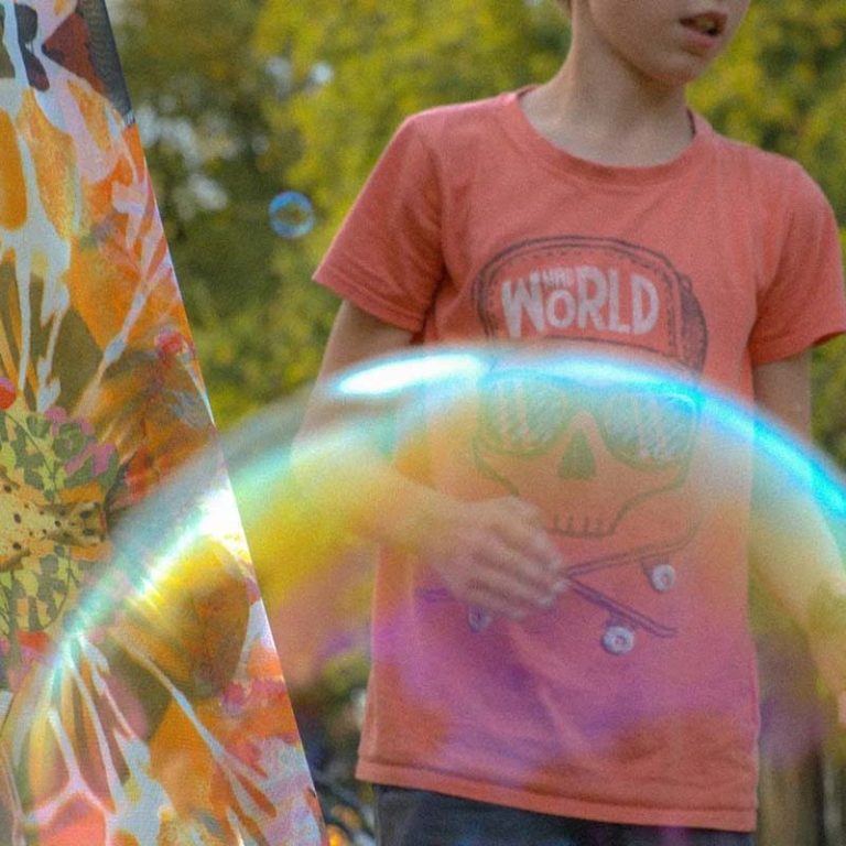 Een jongen met een T-shirt aan staat buiten naast een grote zeepbel.